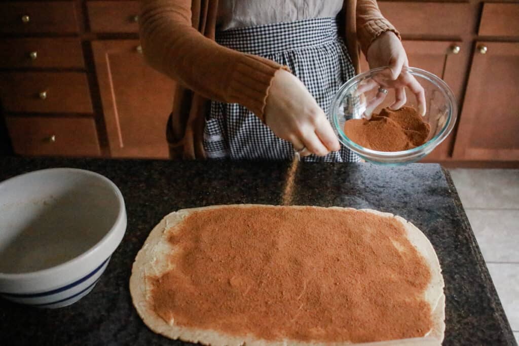 Woman sprinkling coconut sugar in cinnamon roll filling