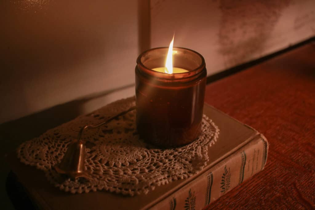 Candle lit in dim room on top of a doily on top of a book
