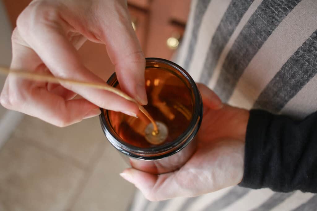 Woman placing candle wick in the center of a candle vessel
