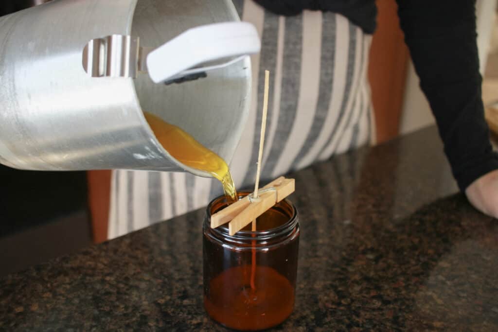 Woman pouring hot candle wax into prepared candle vessel jar
