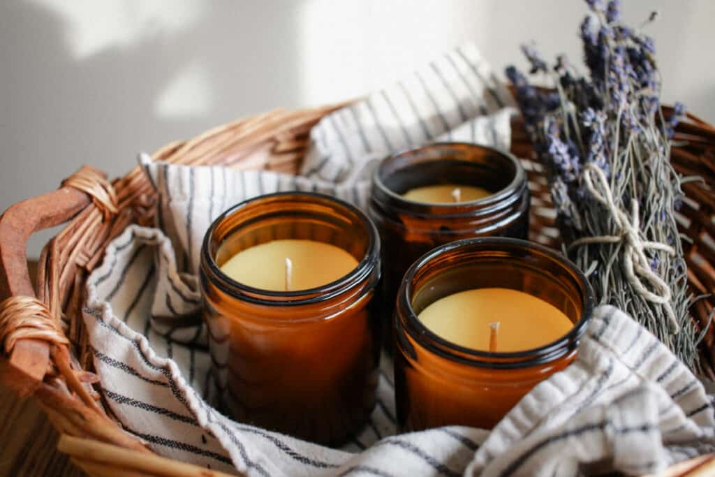 3 beeswax candles in brown vessels on a towerl in a basket