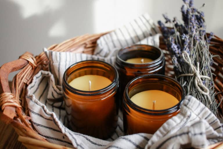 3 beeswax candles in brown vessels on a towerl in a basket