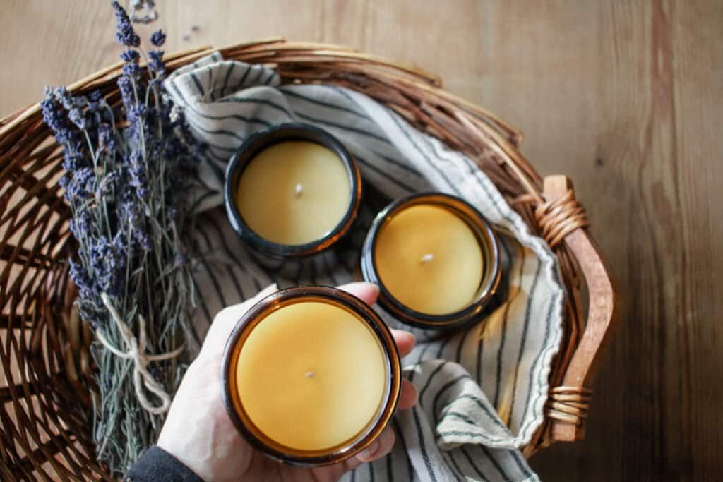 Woman holding freshly poured beeswax candles in a basket with a towel and bundle of lavender