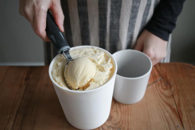woman scooping vanilla ice cream out of quart containter