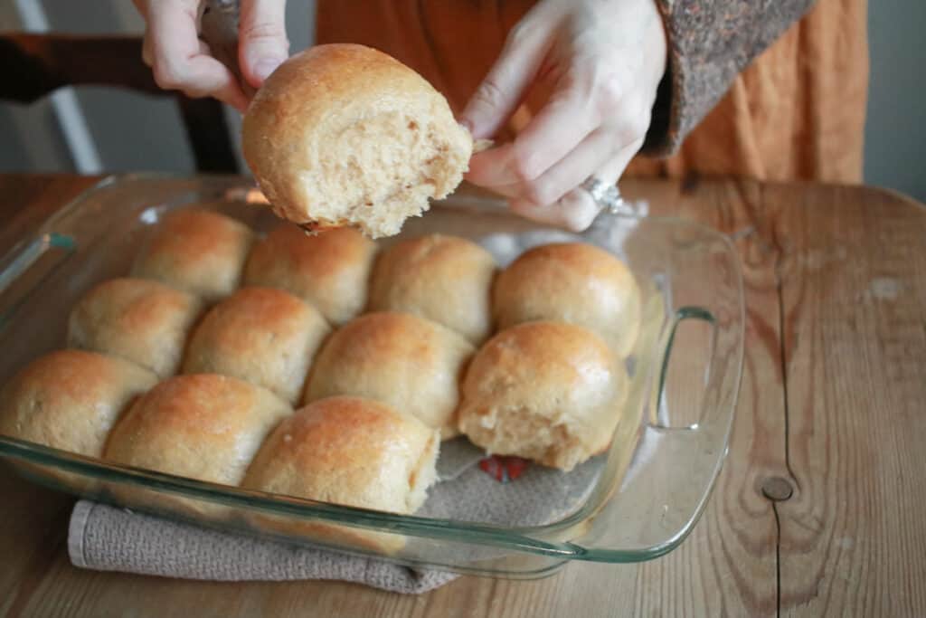 Pan of sourdough dinner rolls with woman holding one on a spatula